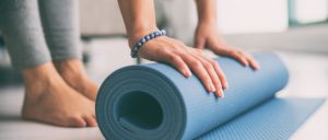 aufgerollte Yogamatte liegt am Boden. Eine person beugt sich über die Matte und legt die Hände auf die Matte SHBB Bad Oldesloe